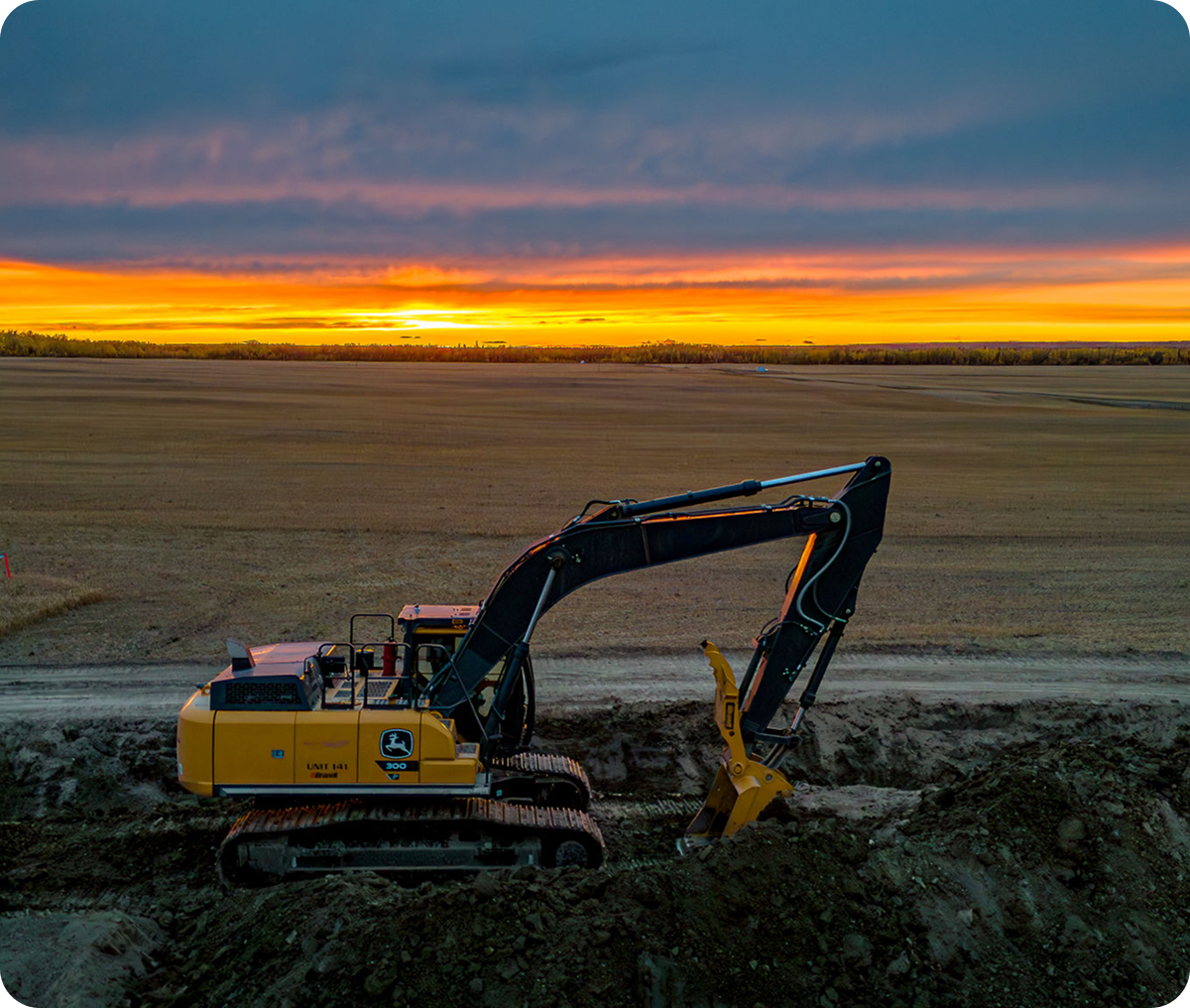 Digger on dirt field at sunset