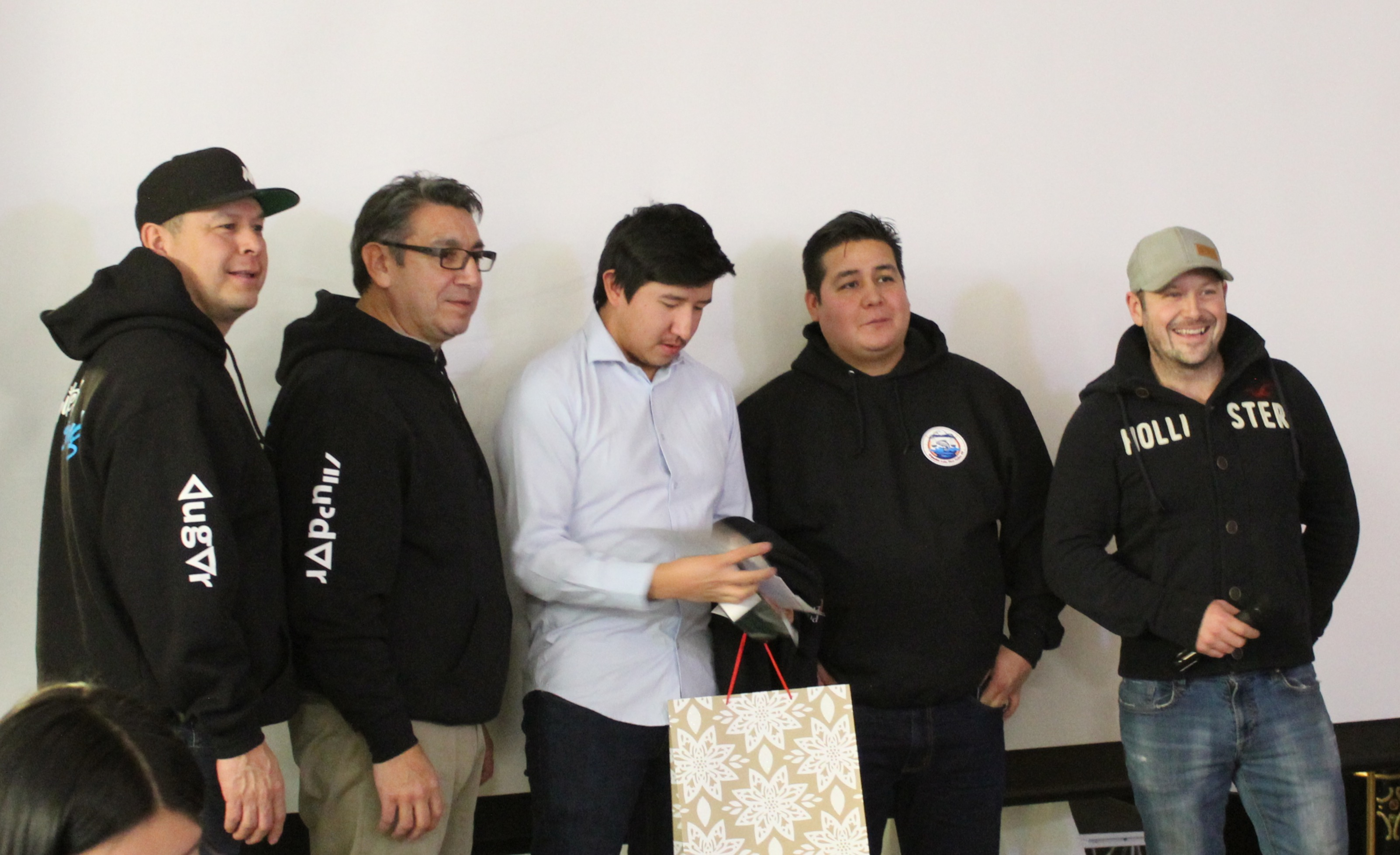 Four men standing together, with one handing a gift bag.