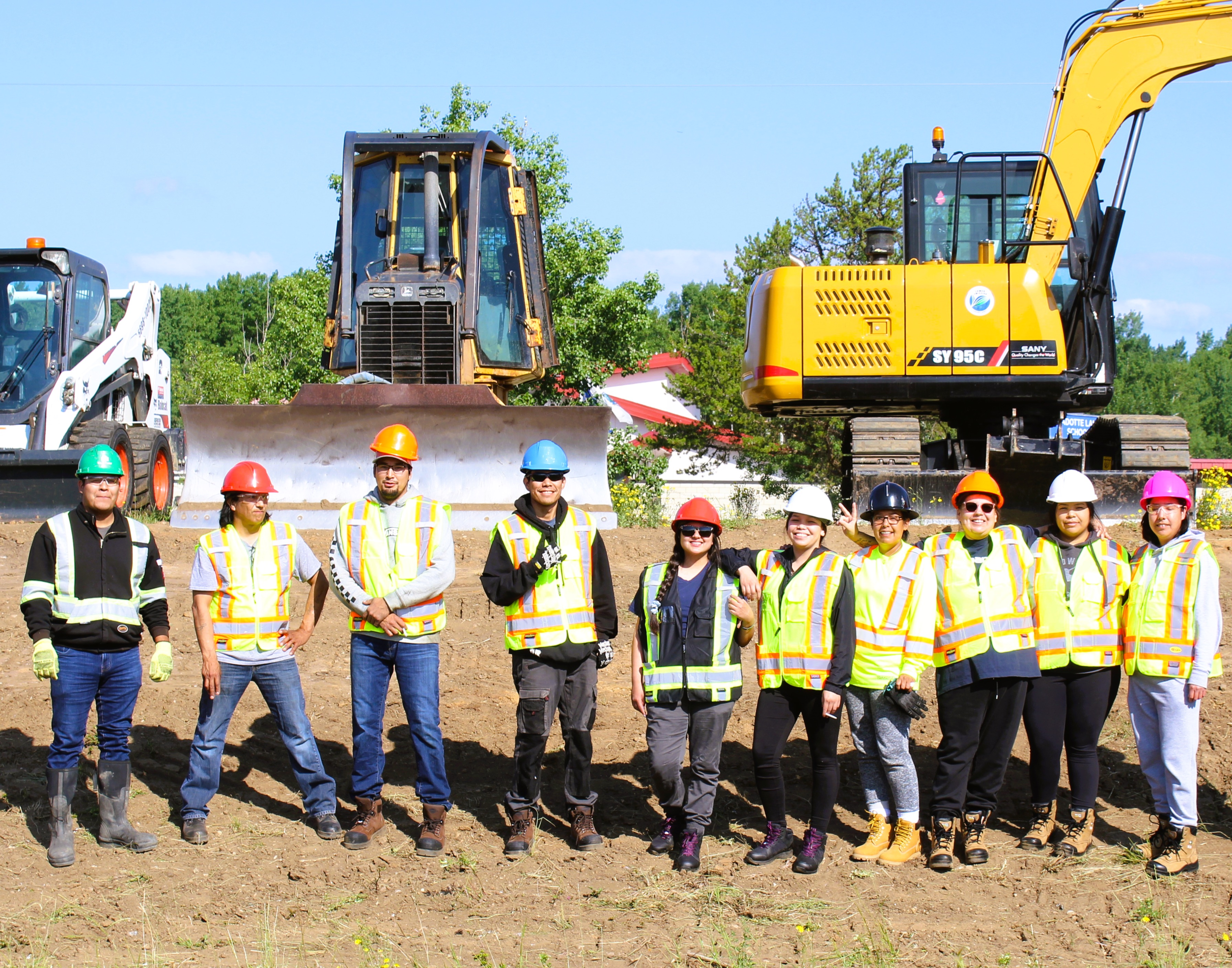 Construction workers stand in front of heavy machinery on a worksite.