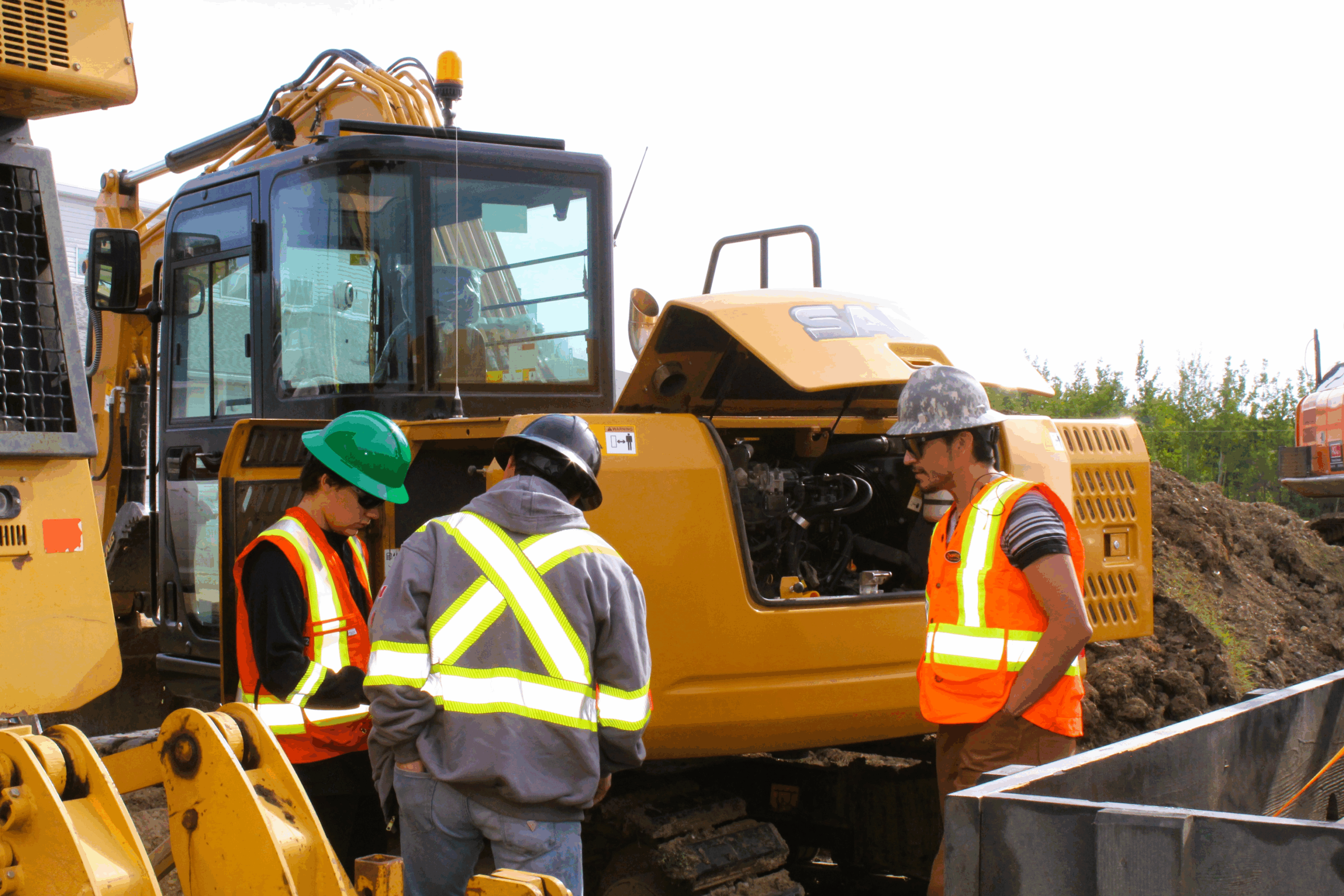 Construction workers examining equipment near a yellow excavator.