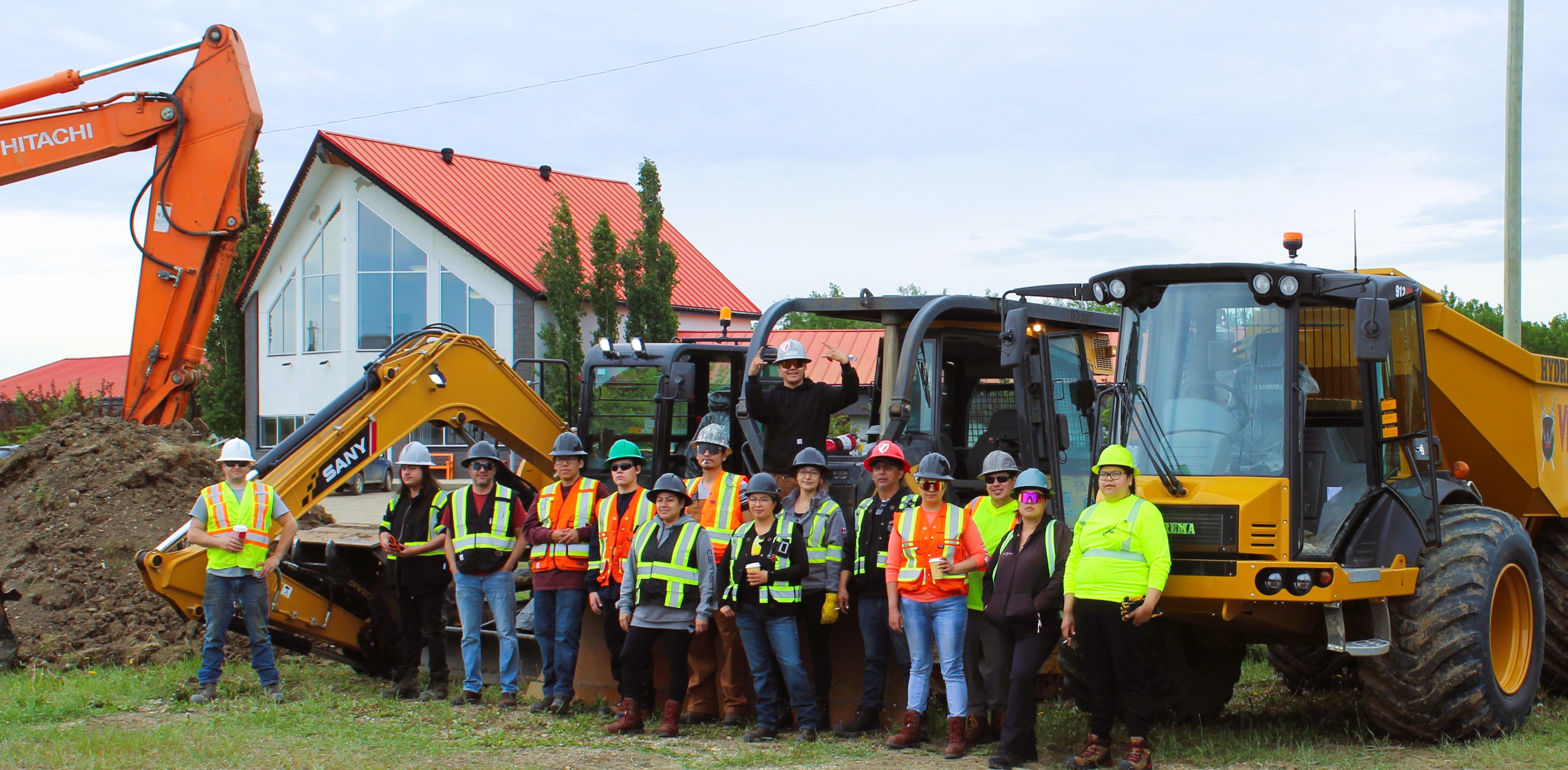 Construction workers stand in a line with heavy machinery behind them.