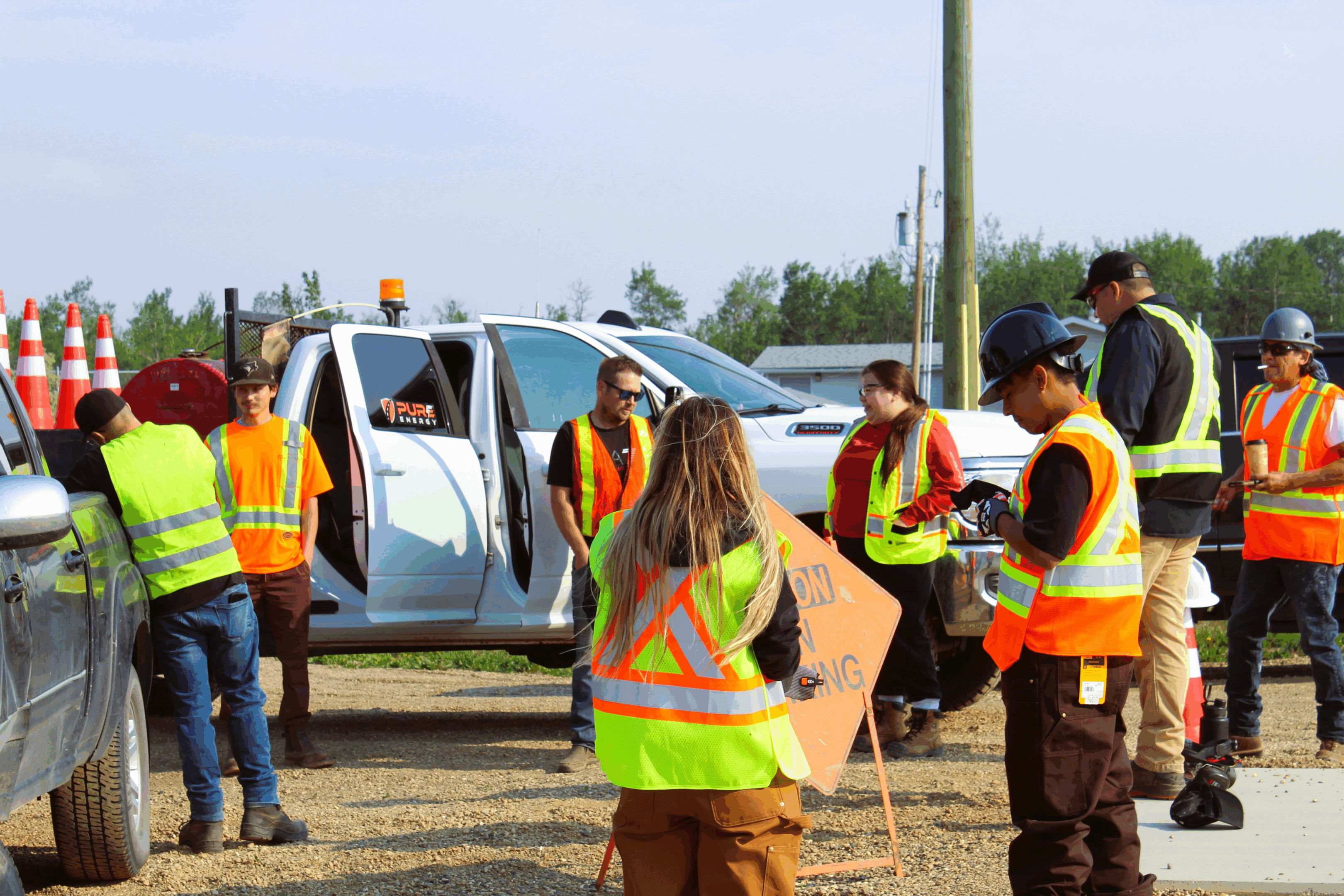 Workers in safety vests gather near a truck outdoors.