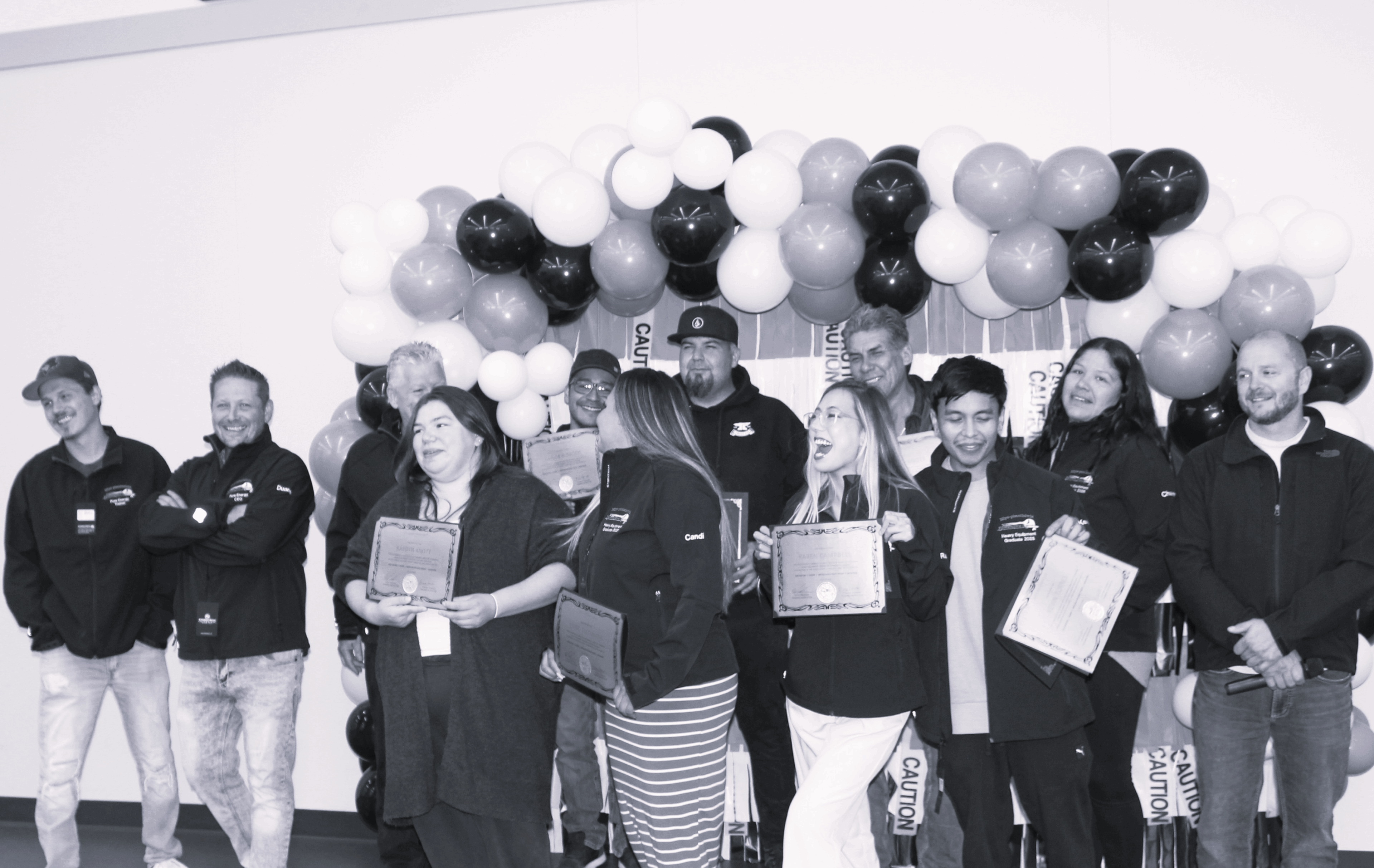 Group of people holding certificates in front of black, white, and gray balloons.